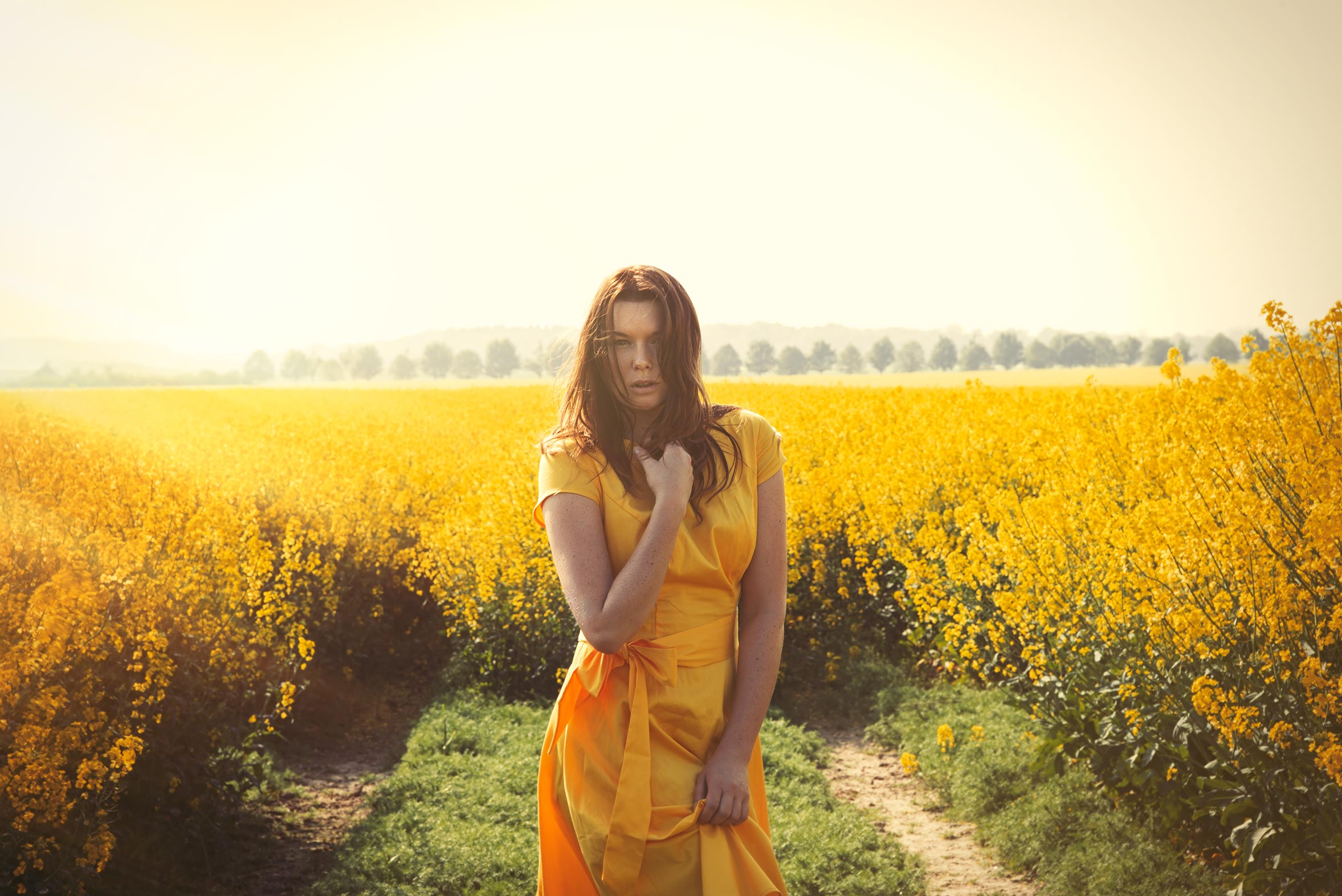 Frau in einem gelben Rapsfeld die Fotografiert wird mit einem gelben Kleid